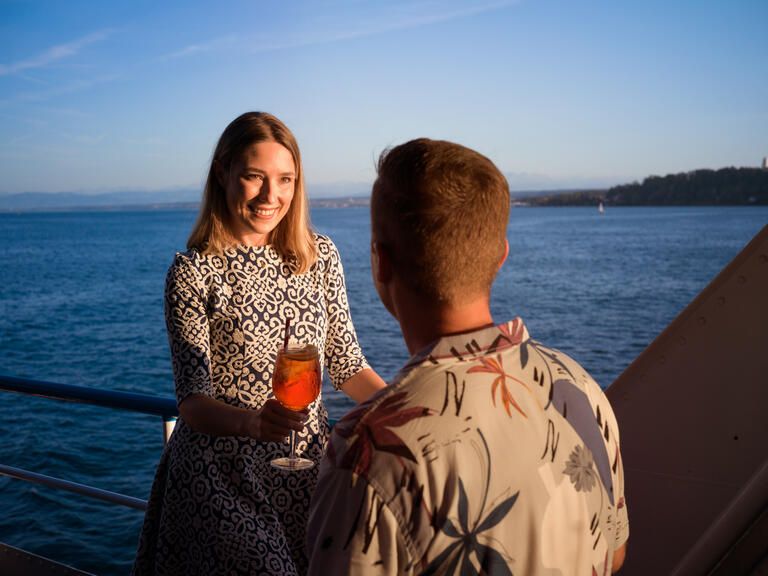 Eine Frau und ein Mann stoßen mit einem Glas auf einem Schiff an.