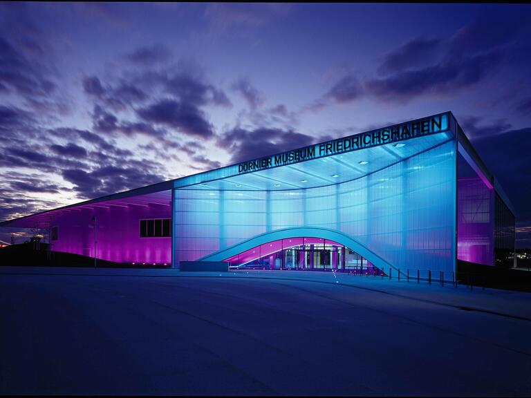 Das Dornier Museum von außen, blau beleuchtet. 